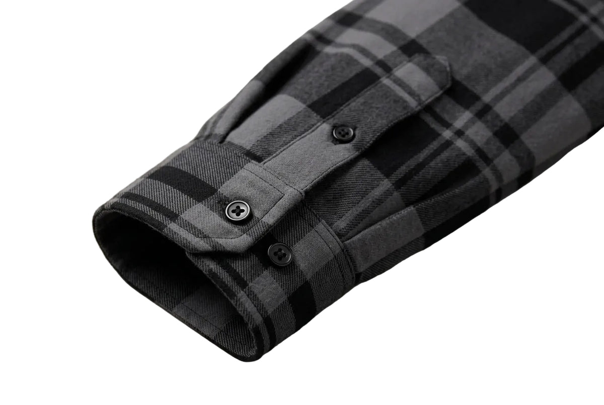 Close-up of a plaid long-sleeve shirt cuff in black, gray, and white, featuring a buttoned flap pocket.